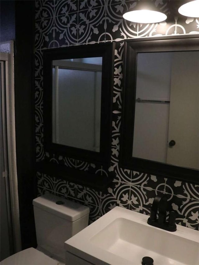 half bathroom featuring toilet, vanity, and wallpapered walls