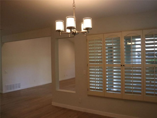 empty room featuring wood finished floors, visible vents, baseboards, and an inviting chandelier