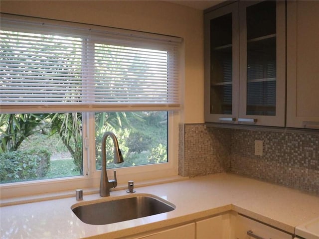kitchen featuring glass insert cabinets, a sink, backsplash, and a healthy amount of sunlight