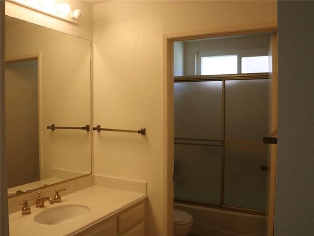 full bath featuring combined bath / shower with glass door, toilet, and vanity
