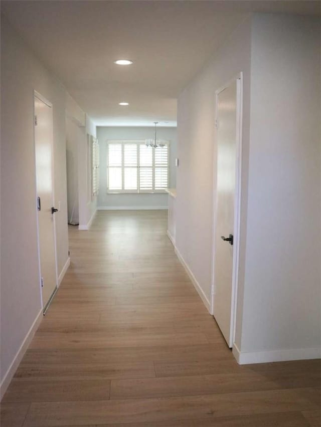 hall with wood finished floors, baseboards, recessed lighting, and a chandelier