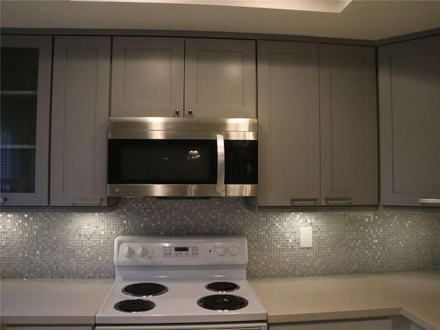 kitchen with stainless steel microwave, backsplash, gray cabinets, light countertops, and white range with electric stovetop