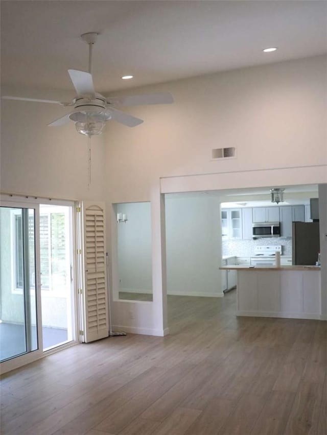 unfurnished living room with light wood-type flooring, visible vents, recessed lighting, a ceiling fan, and a high ceiling
