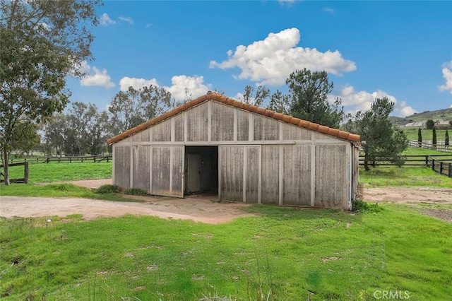 view of outbuilding with an outdoor structure, a rural view, and fence