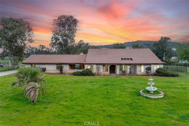 view of front of home featuring a tile roof, a lawn, stucco siding, and fence