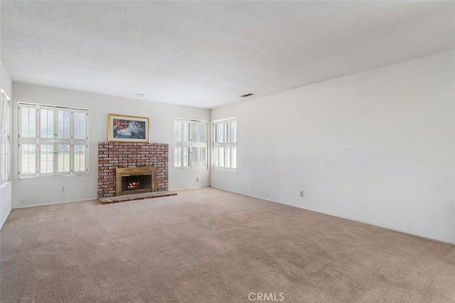 unfurnished living room featuring a brick fireplace, visible vents, and carpet