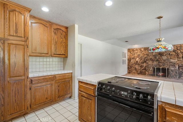 kitchen featuring hanging light fixtures, tile counters, backsplash, light tile patterned flooring, and black electric range oven
