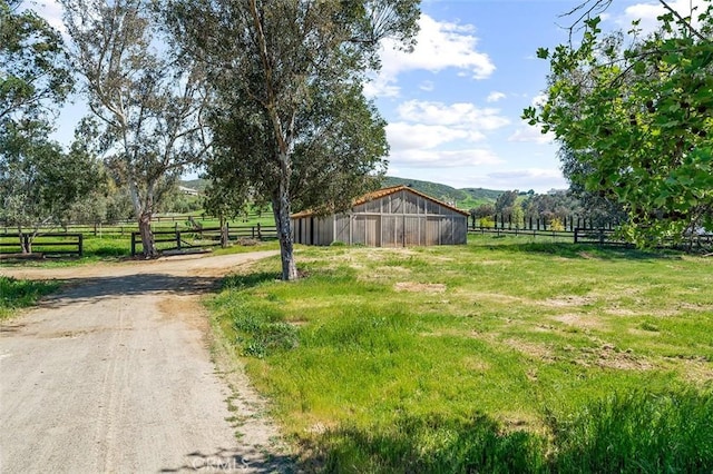 view of yard with fence, an outdoor structure, and a rural view