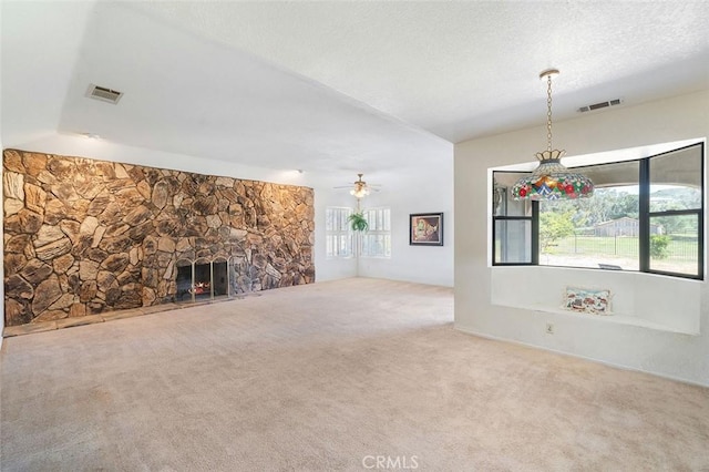 unfurnished living room featuring carpet, visible vents, a ceiling fan, and a stone fireplace