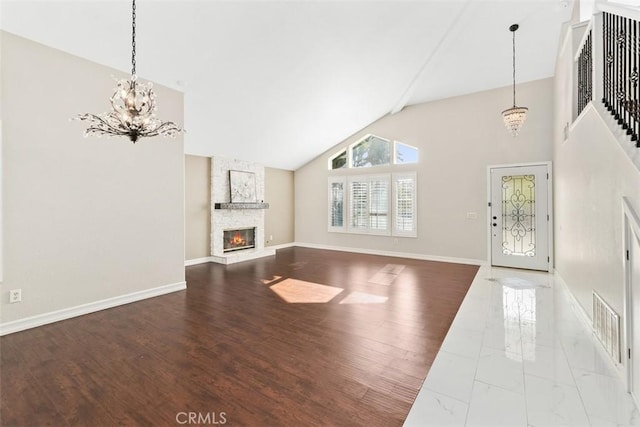 unfurnished living room with a fireplace, a notable chandelier, baseboards, and wood finished floors
