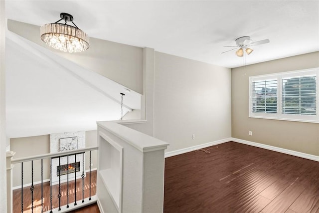 spare room featuring baseboards, wood finished floors, and ceiling fan with notable chandelier