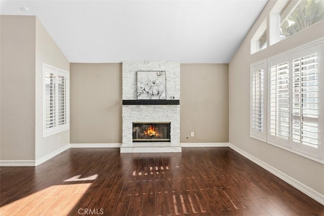 unfurnished living room with wood-type flooring, a stone fireplace, baseboards, and lofted ceiling
