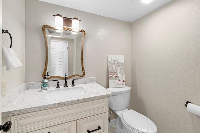 half bathroom with toilet, vanity, and a textured wall