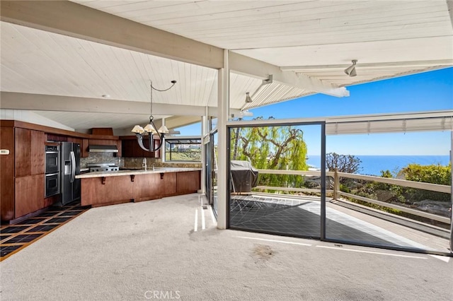 interior space featuring a kitchen bar, dark colored carpet, under cabinet range hood, a chandelier, and vaulted ceiling with beams