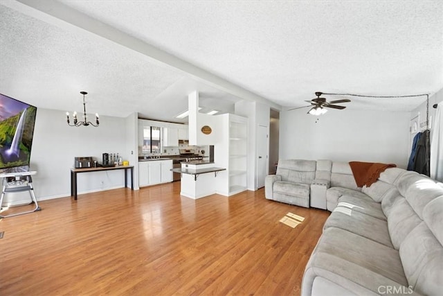 living room featuring a textured ceiling, ceiling fan with notable chandelier, baseboards, and light wood-type flooring