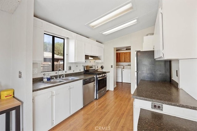 kitchen featuring vaulted ceiling, appliances with stainless steel finishes, a sink, dark countertops, and washing machine and dryer