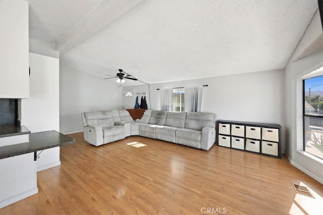 living area with vaulted ceiling, light wood-style flooring, a textured ceiling, visible vents, and ceiling fan