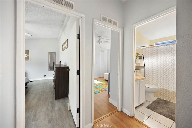 corridor featuring visible vents, baseboards, wood finished floors, and a textured ceiling
