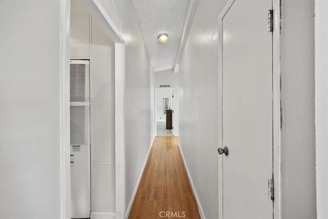 hall with baseboards, a textured ceiling, visible vents, a heating unit, and wood finished floors