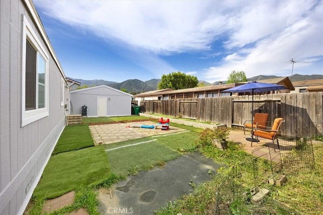 view of yard featuring a patio area, a mountain view, a fenced backyard, and an outbuilding