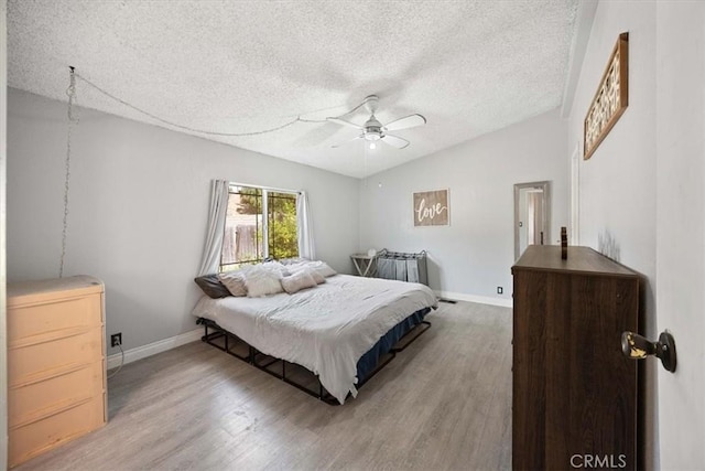 bedroom featuring lofted ceiling, baseboards, a textured ceiling, and wood finished floors