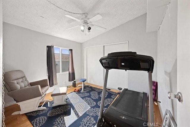 exercise room with baseboards, vaulted ceiling, a textured ceiling, ceiling fan, and wood finished floors