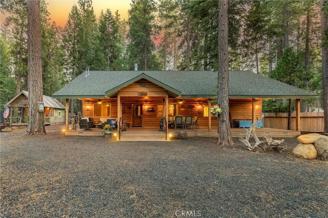 rustic home featuring a porch, fence, and roof with shingles