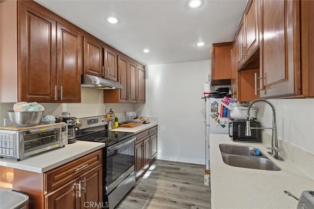 kitchen with light countertops, under cabinet range hood, stainless steel electric range oven, and a sink