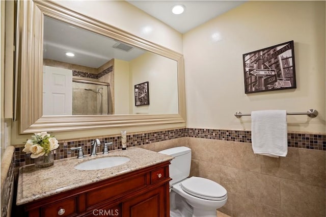 bathroom with visible vents, toilet, tile walls, a shower stall, and vanity
