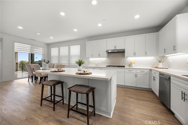 kitchen featuring a breakfast bar, a center island, white cabinetry, under cabinet range hood, and dishwasher