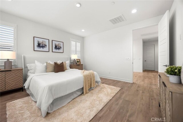 bedroom with baseboards, recessed lighting, wood finished floors, and visible vents