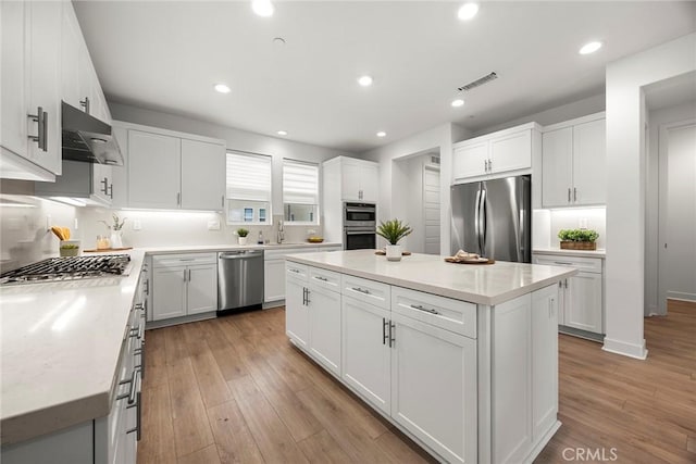 kitchen featuring light wood-style flooring, a center island, stainless steel appliances, under cabinet range hood, and visible vents