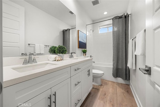 full bathroom featuring double vanity, visible vents, wood finished floors, shower / tub combo, and a sink