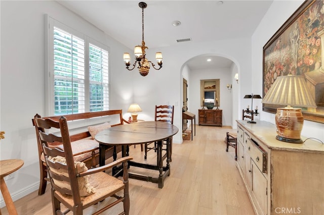 dining space with arched walkways, visible vents, a chandelier, and light wood finished floors