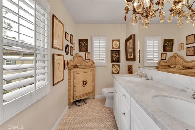 bathroom with double vanity, a sink, toilet, and a notable chandelier