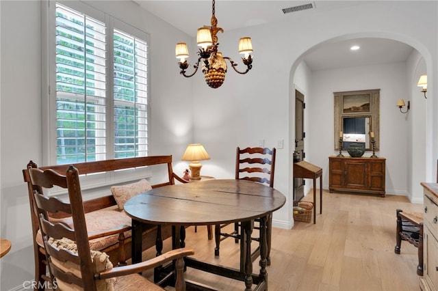 dining space with visible vents, a notable chandelier, arched walkways, and light wood-style floors