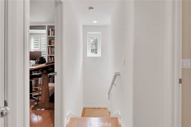 hall featuring baseboards, wood finished floors, and a healthy amount of sunlight
