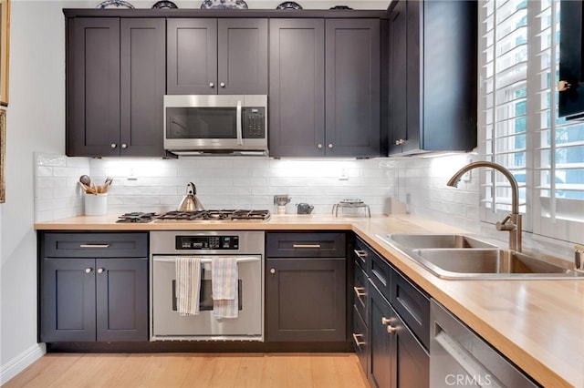 kitchen with decorative backsplash, light countertops, light wood finished floors, appliances with stainless steel finishes, and a sink