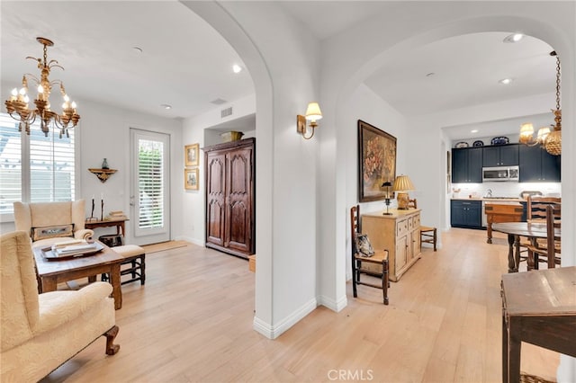 interior space featuring a chandelier, light wood-type flooring, baseboards, arched walkways, and recessed lighting