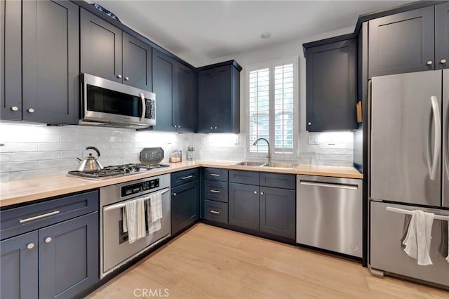 kitchen with light wood-type flooring, stainless steel appliances, decorative backsplash, a sink, and butcher block counters