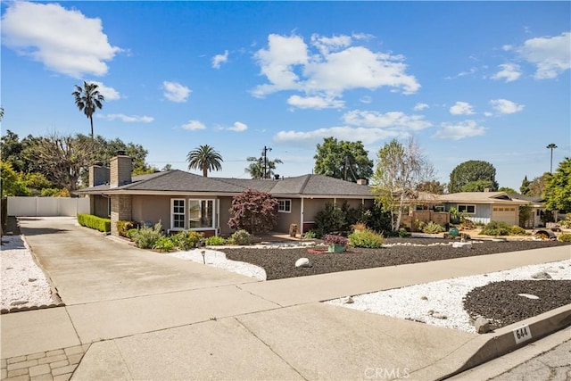single story home with concrete driveway, stucco siding, fence, and a chimney