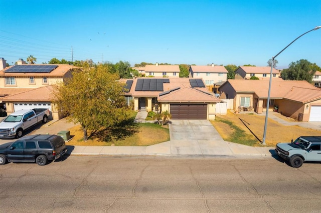 traditional home featuring a residential view, a front lawn, solar panels, concrete driveway, and an attached garage