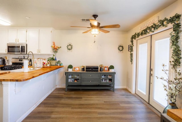 kitchen with white cabinets, dark wood-style floors, stainless steel appliances, visible vents, and wood counters
