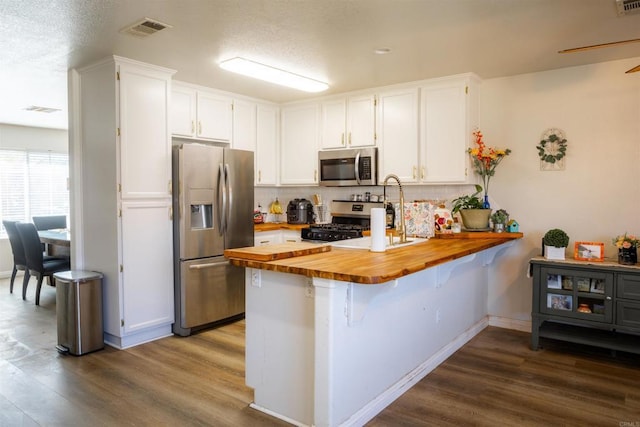 kitchen featuring a peninsula, dark wood-style flooring, visible vents, wood counters, and appliances with stainless steel finishes