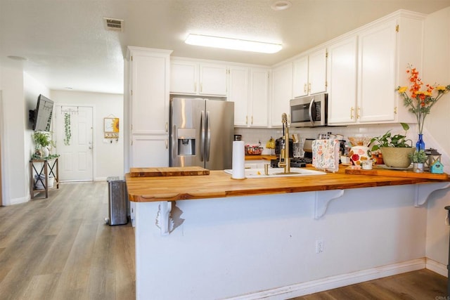 kitchen with a peninsula, butcher block counters, white cabinetry, and stainless steel appliances