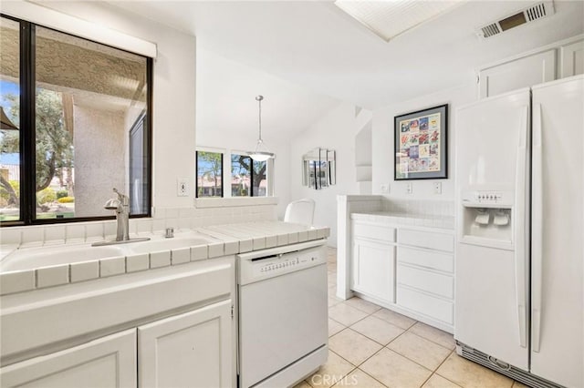 kitchen with a sink, tile countertops, light tile patterned floors, white appliances, and visible vents