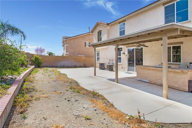 rear view of house with an outdoor kitchen, ceiling fan, a fenced backyard, stucco siding, and a patio