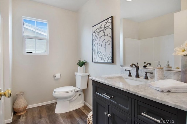 bathroom featuring toilet, vanity, wood finished floors, and baseboards