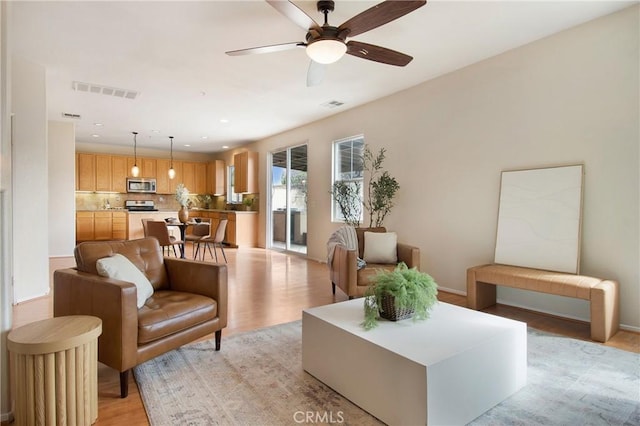 living area featuring light wood-style flooring, a ceiling fan, and visible vents