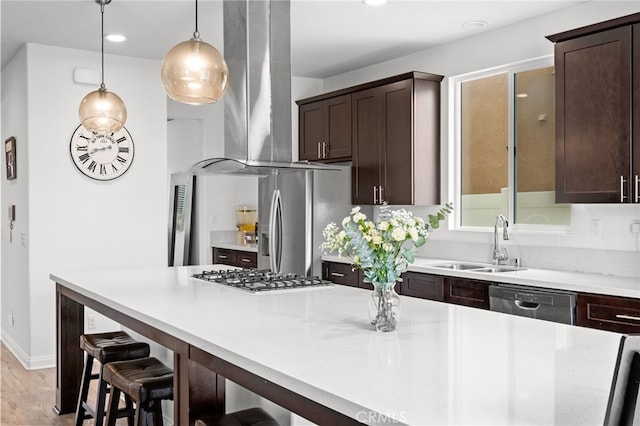 kitchen featuring wall chimney range hood, light countertops, dark brown cabinets, appliances with stainless steel finishes, and a sink